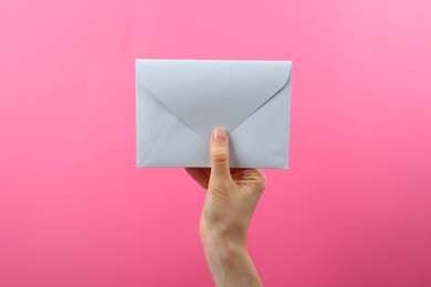 Woman holding white paper envelope on pink background, closeup