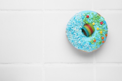 Photo of Glazed donut decorated with sprinkles on white tiled table, top view. Space for text. Tasty confectionery