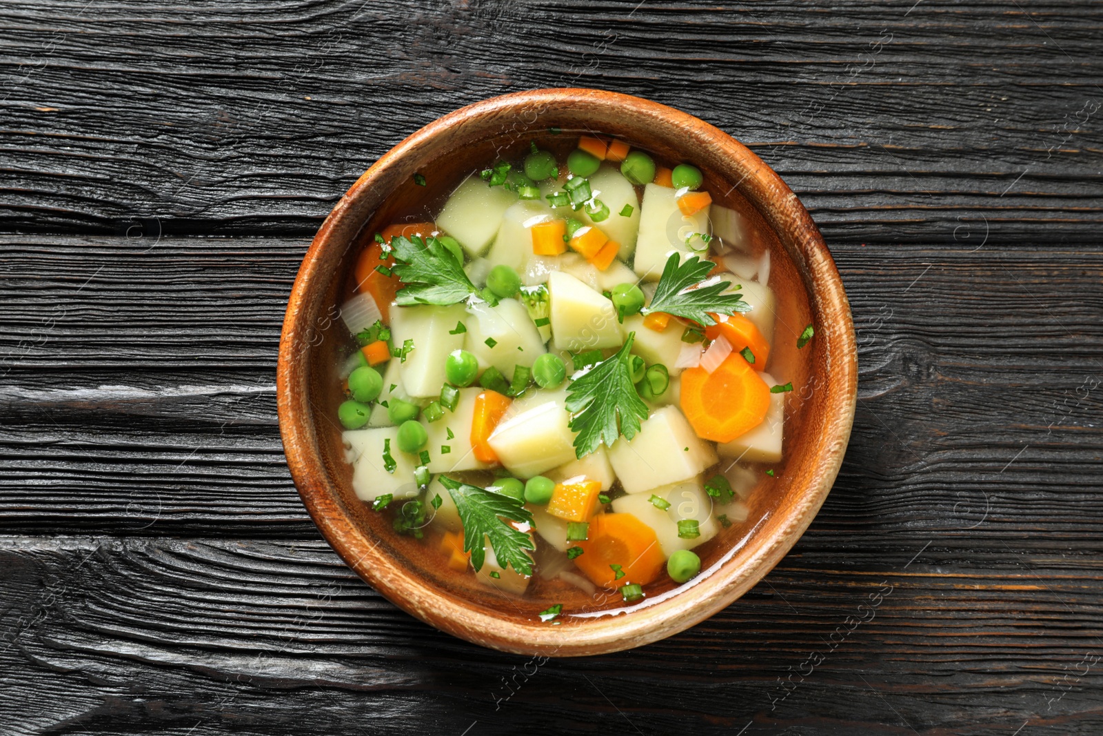 Photo of Bowl of fresh homemade vegetable soup on dark wooden background, top view