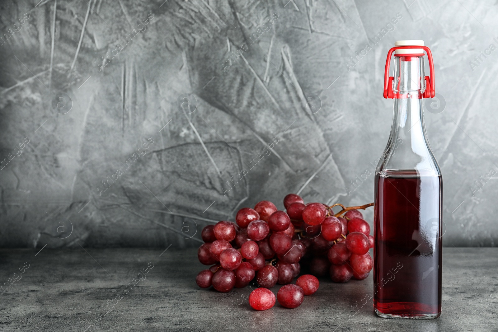 Photo of Bottle with wine vinegar and fresh grapes on gray table. Space for text