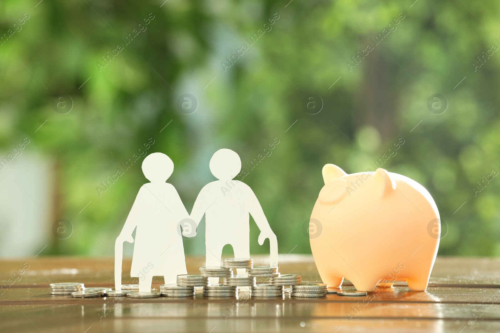 Photo of Pension savings. Figure of senior couple, piggy bank and coins on wooden table outdoors