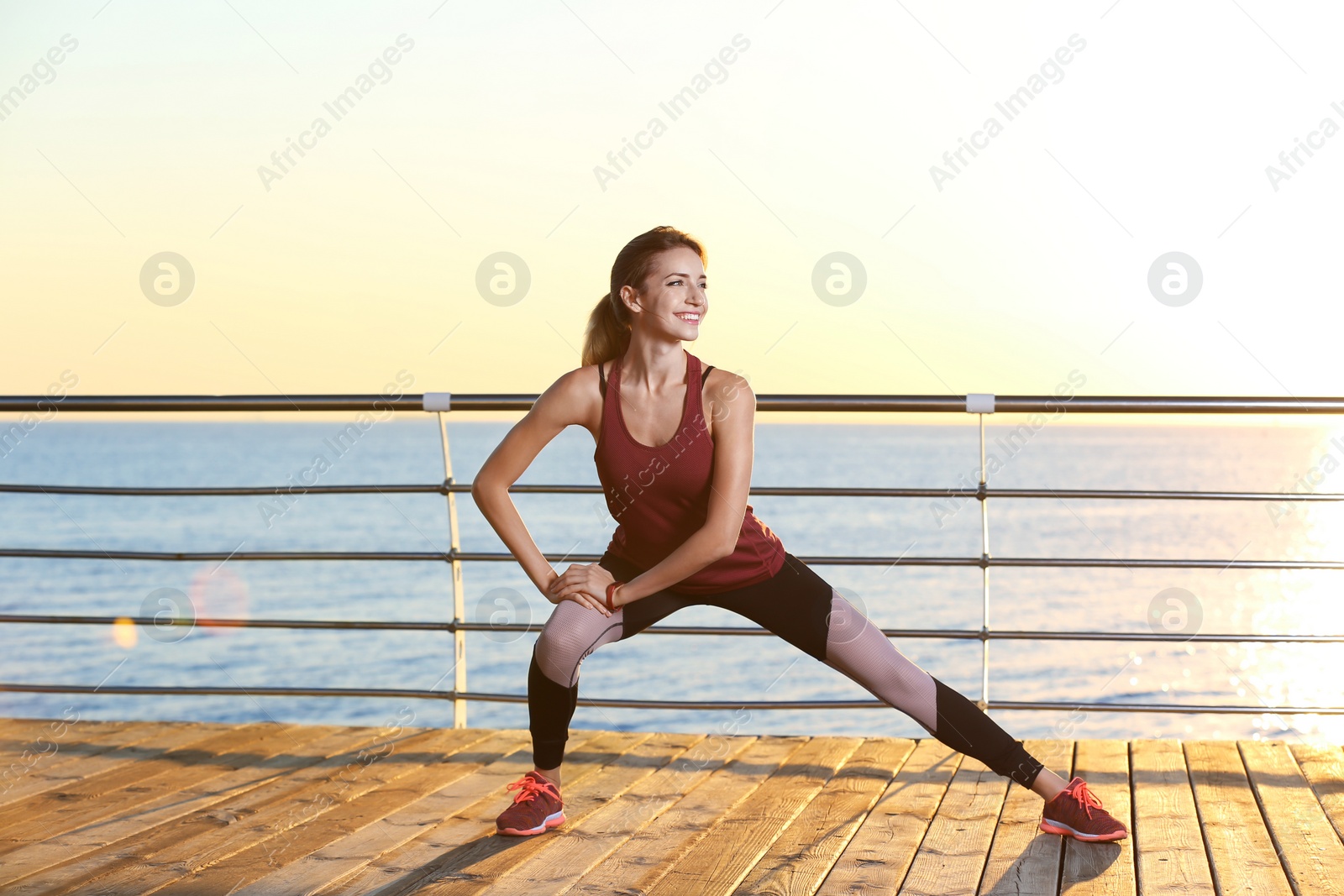 Photo of Young woman doing fitness exercises on pier in morning