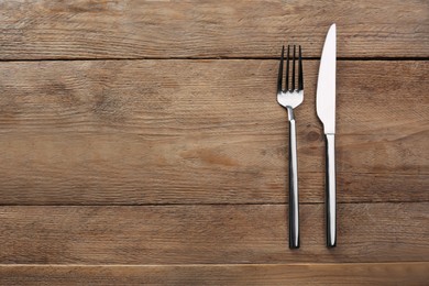 Fork and knife on wooden table, flat lay with space for text. Stylish shiny cutlery set