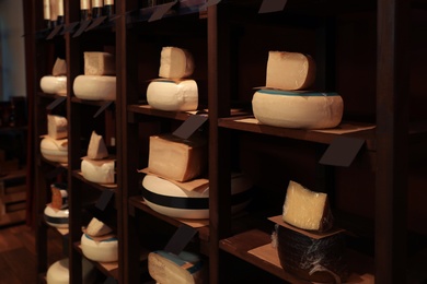 Photo of Different types of delicious cheeses on rack in store