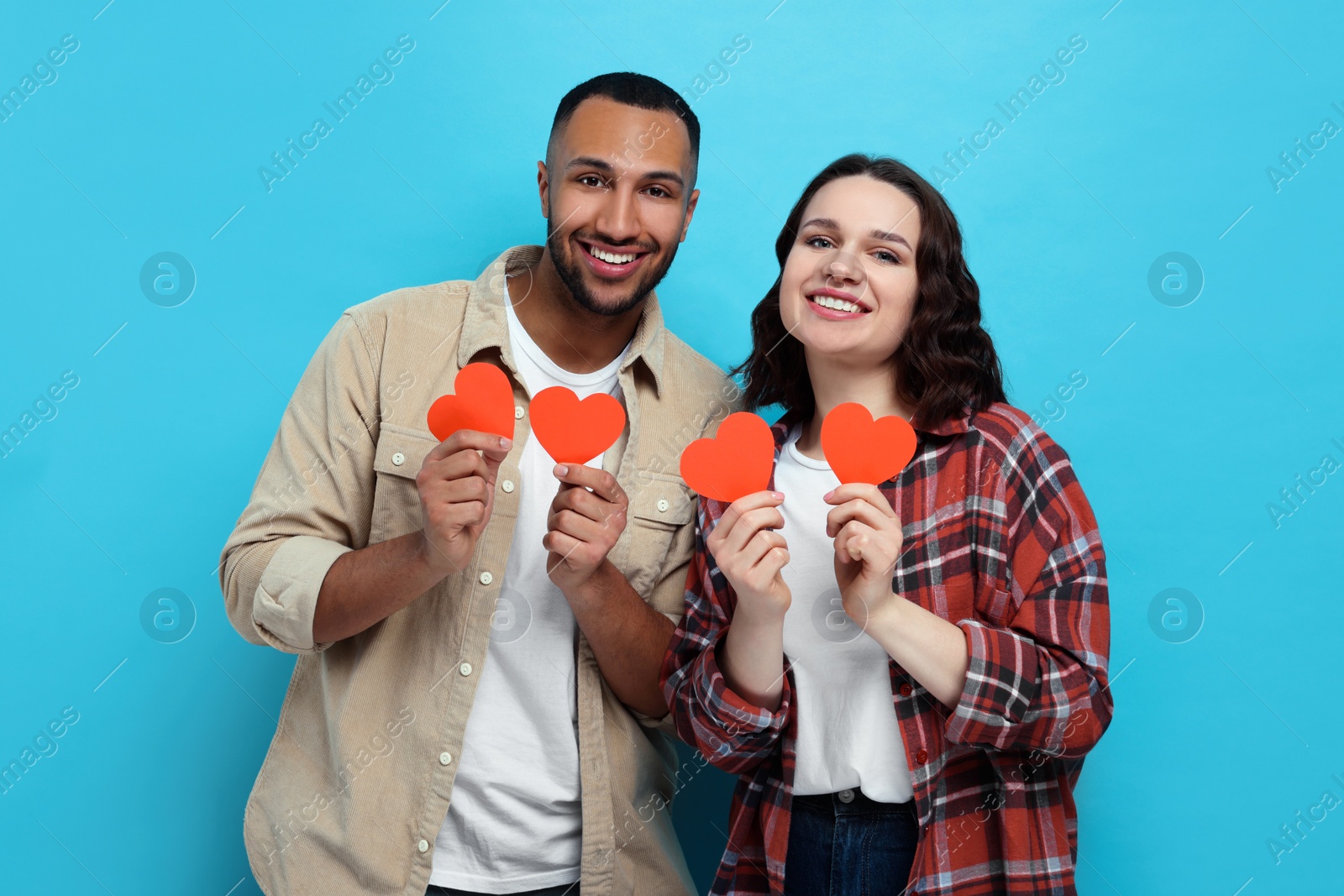 Photo of Lovely couple with red paper hearts on light blue background. Valentine's day celebration