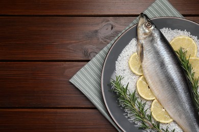 Photo of Delicious salted herring, rosemary, salt and lemon on wooden table, top view. Space for text