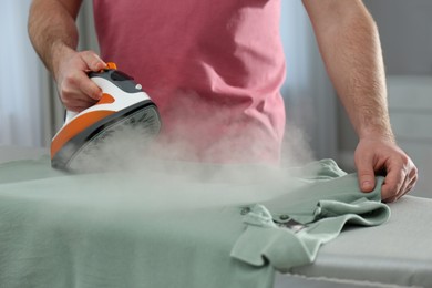 Photo of Man ironing clean shirt at home, closeup