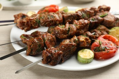 Metal skewers with delicious meat and vegetables served on white wooden table, closeup