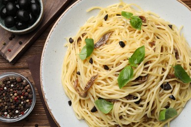 Photo of Delicious pasta with anchovies, olives and basil on wooden table, flat lay