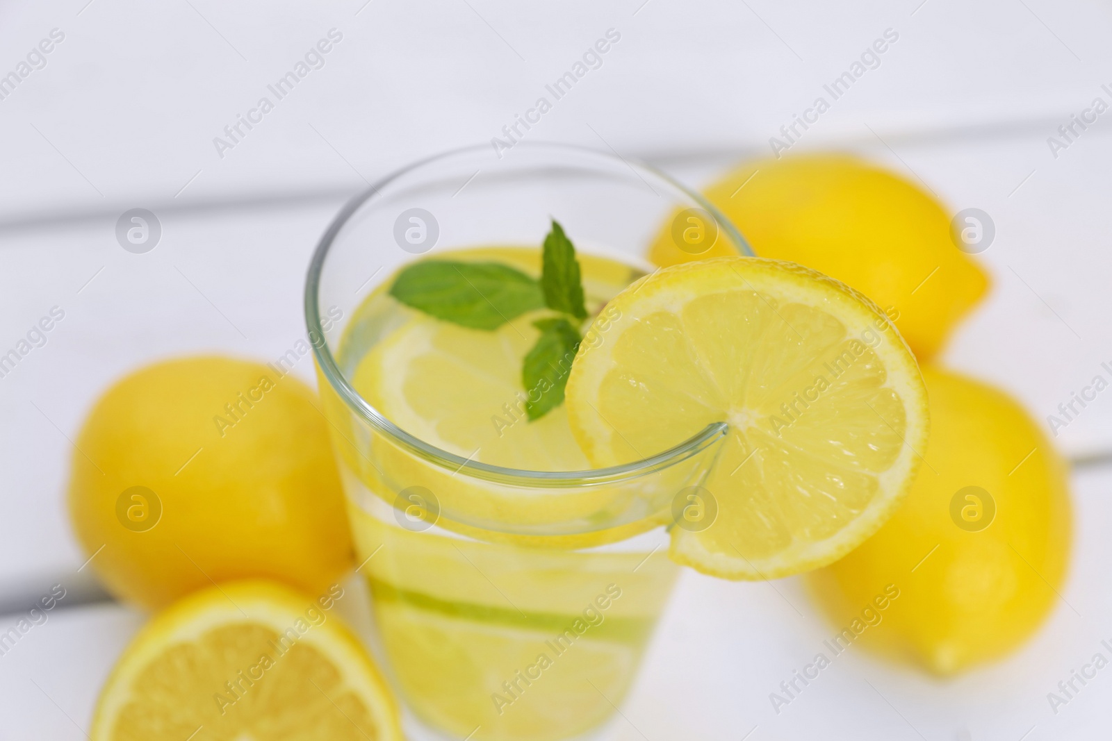 Photo of Glass of water with lemons and mint on white wooden table, closeup
