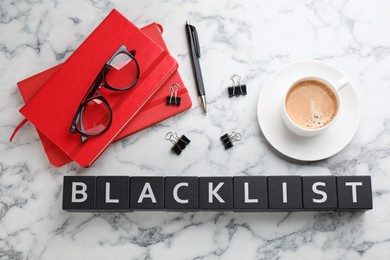 Black wooden cubes with word Blacklist, cup of coffee and office stationery on white marble table, flat lay
