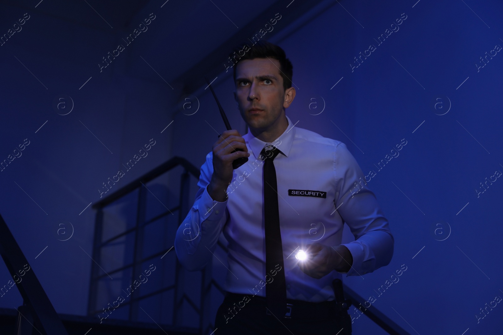 Photo of Male security guard with flashlight and portable radio transmitter in dark room