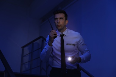 Photo of Male security guard with flashlight and portable radio transmitter in dark room