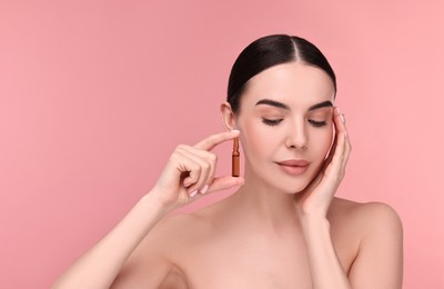 Photo of Beautiful young woman holding skincare ampoule on pink background