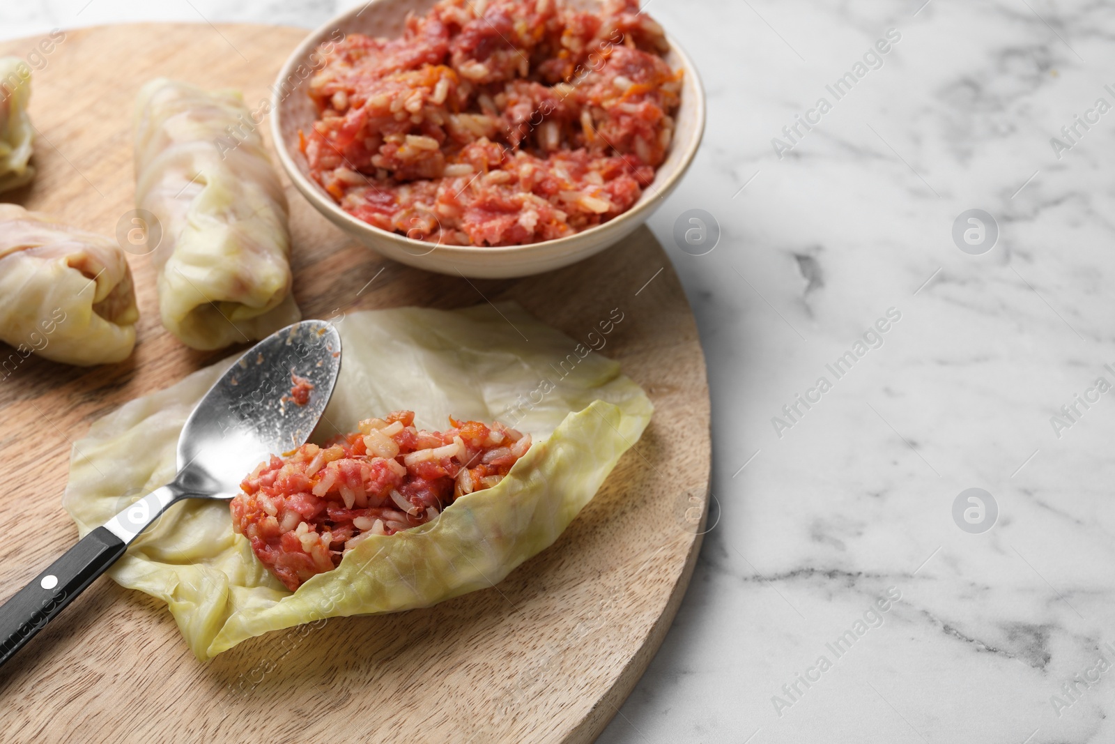 Photo of Preparing stuffed cabbage rolls on white marble table. Space for text