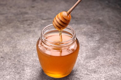 Photo of Pouring sweet golden honey from dipper into jar at grey textured table