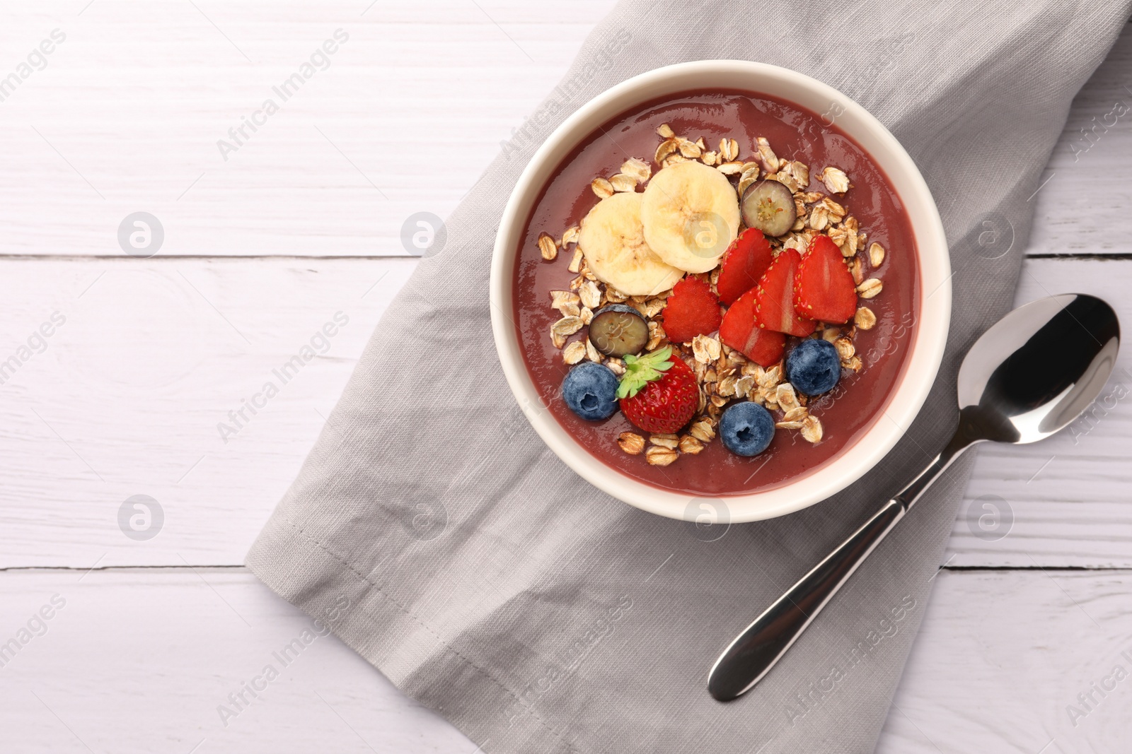 Photo of Delicious smoothie bowl with fresh berries, banana and granola on white wooden table, flat lay. Space for text