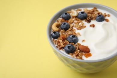 Photo of Bowl with yogurt, blueberries and granola on yellow background, closeup. Space for text