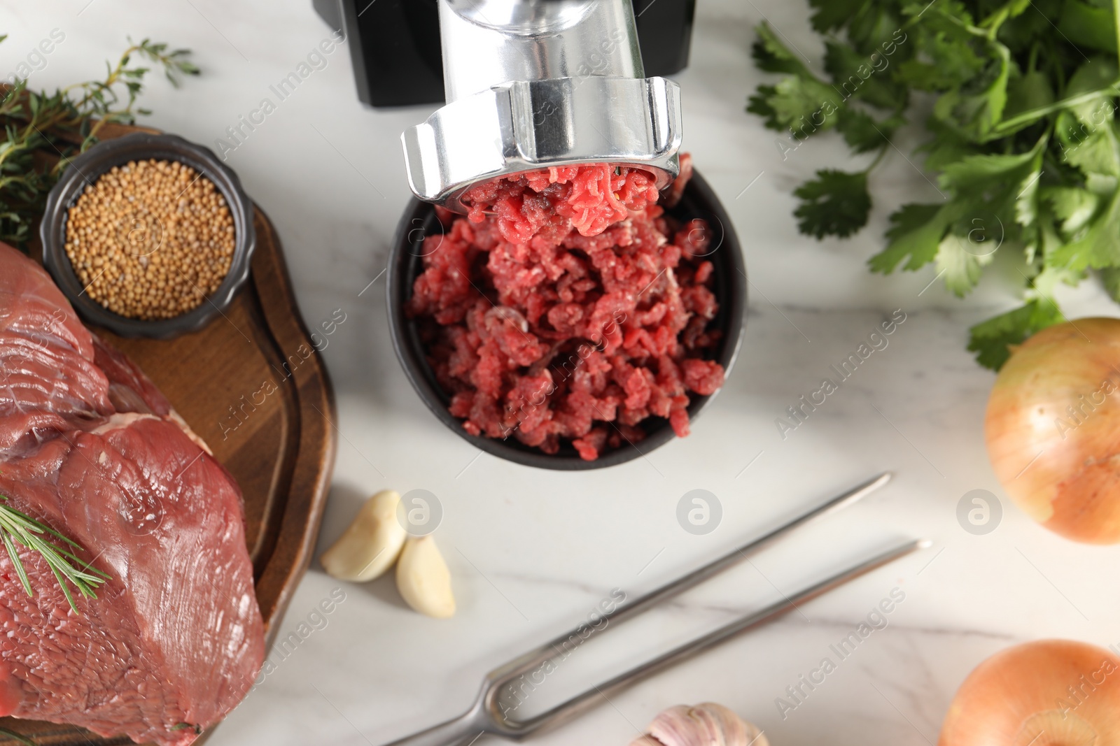 Photo of Electric meat grinder with beef mince and products on white marble table in kitchen, flat lay