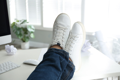 Photo of Lazy office employee resting with feet on desk in office, closeup