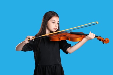 Photo of Preteen girl playing violin on light blue background