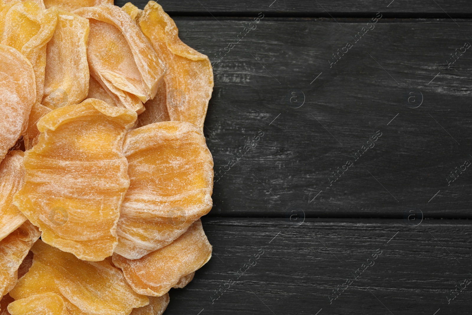 Photo of Delicious dried jackfruit slices on black wooden table, flat lay. Space for text