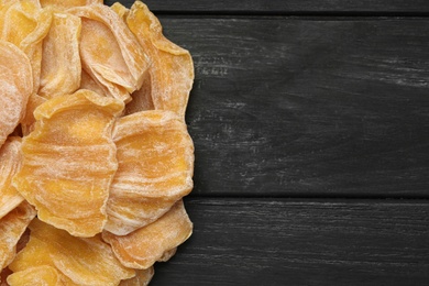 Photo of Delicious dried jackfruit slices on black wooden table, flat lay. Space for text