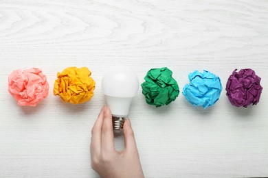 Photo of Woman holding lightbulb among colorful paper balls at white wooden table, top view. Idea concept