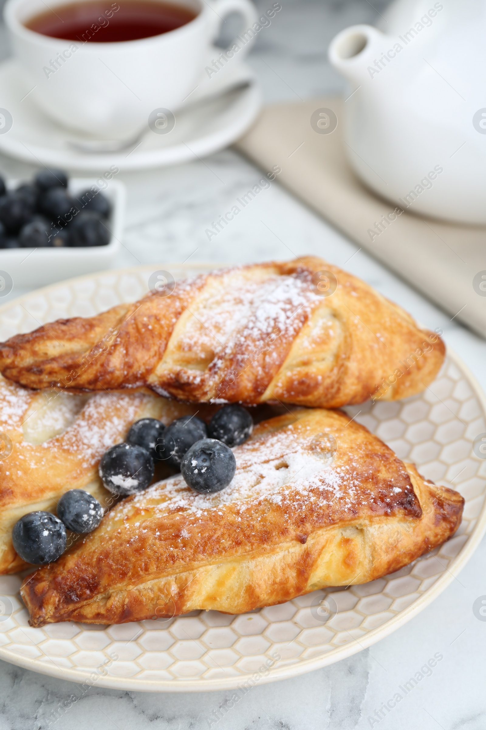 Photo of Fresh tasty puff pastry with sugar powder and blueberries served on white marble table, closeup