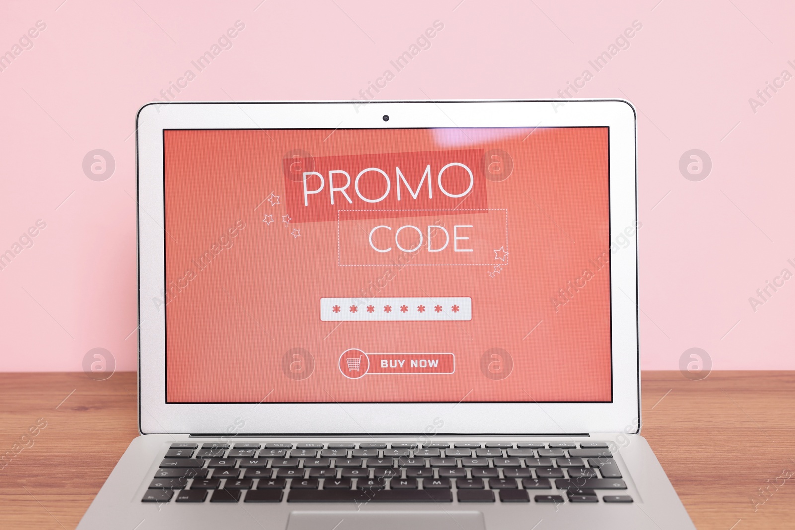 Photo of Laptop with activated promo code on wooden table near pink wall