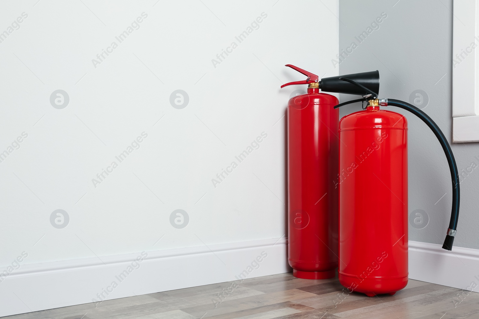 Photo of Fire extinguishers on floor in corner indoors, space for text