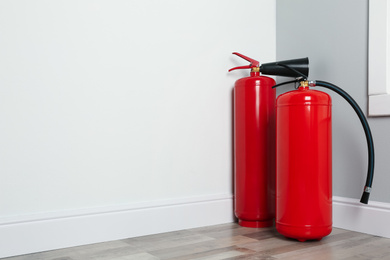 Photo of Fire extinguishers on floor in corner indoors, space for text