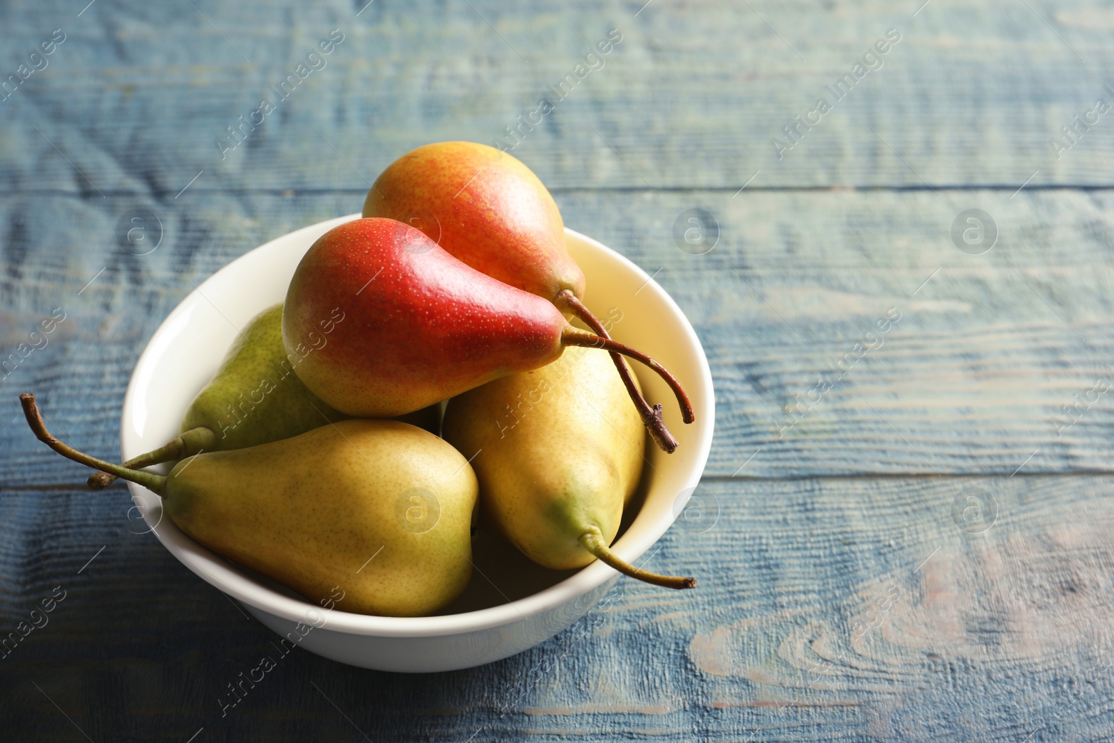 Photo of Bowl with ripe pears on wooden background. Space for text