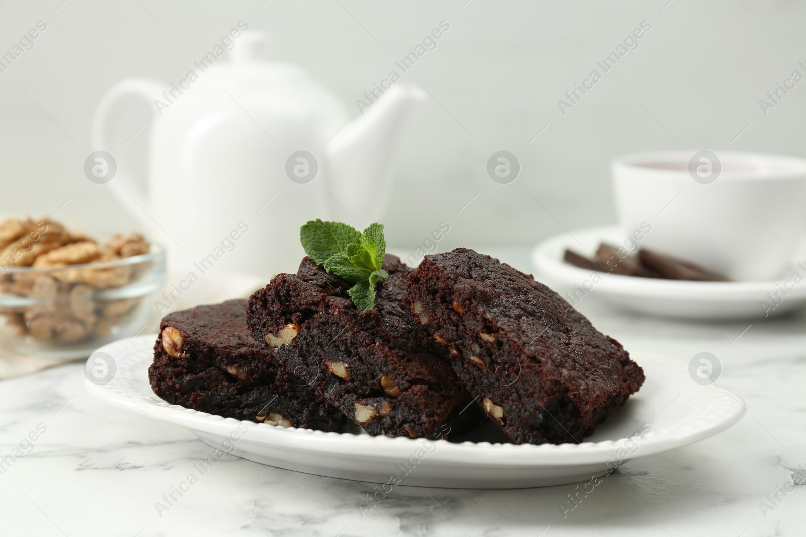 Photo of Delicious brownies with nuts and mint on white marble table. Space for text