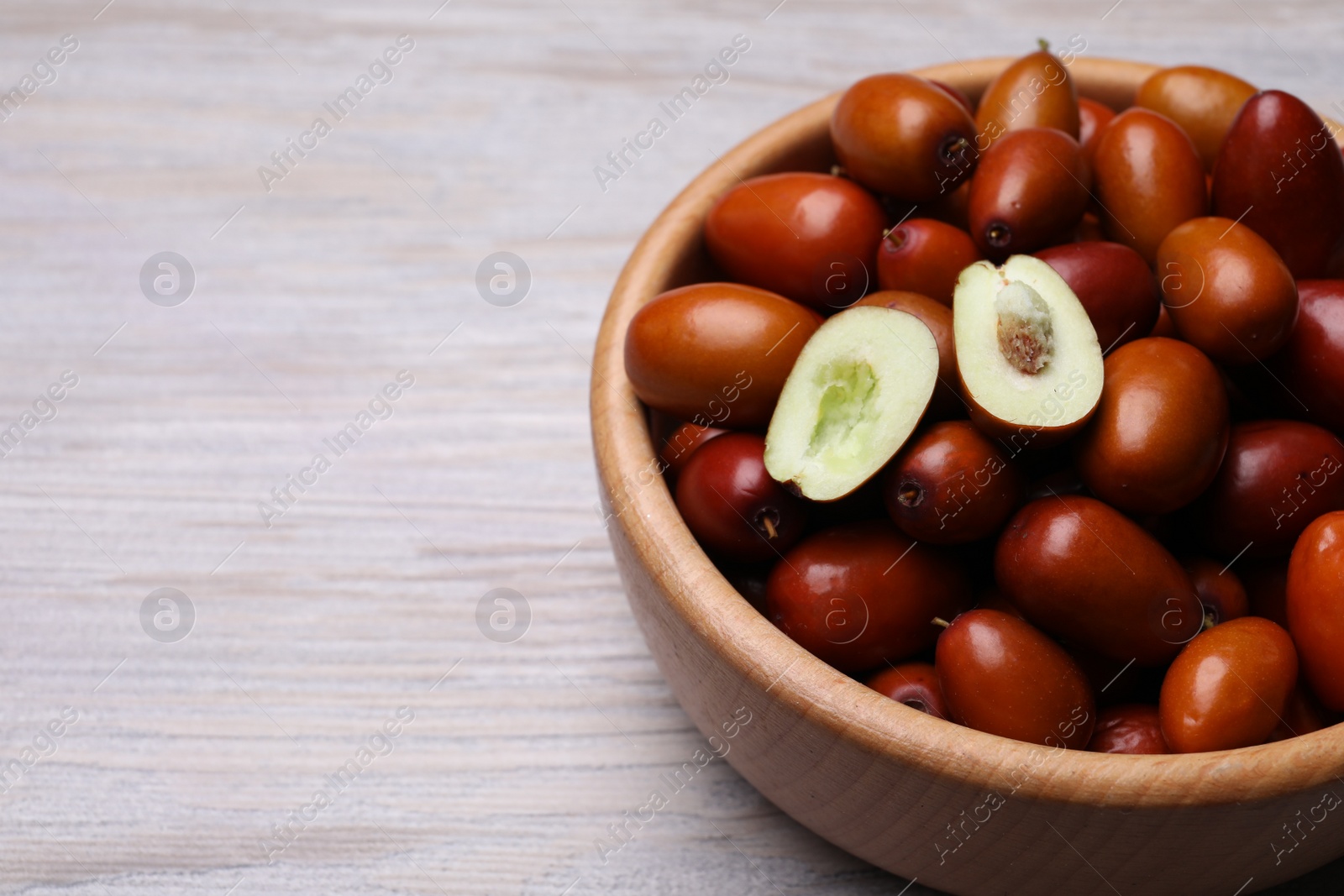 Photo of Fresh Ziziphus jujuba fruits in bowl on wooden table, closeup. Space for text