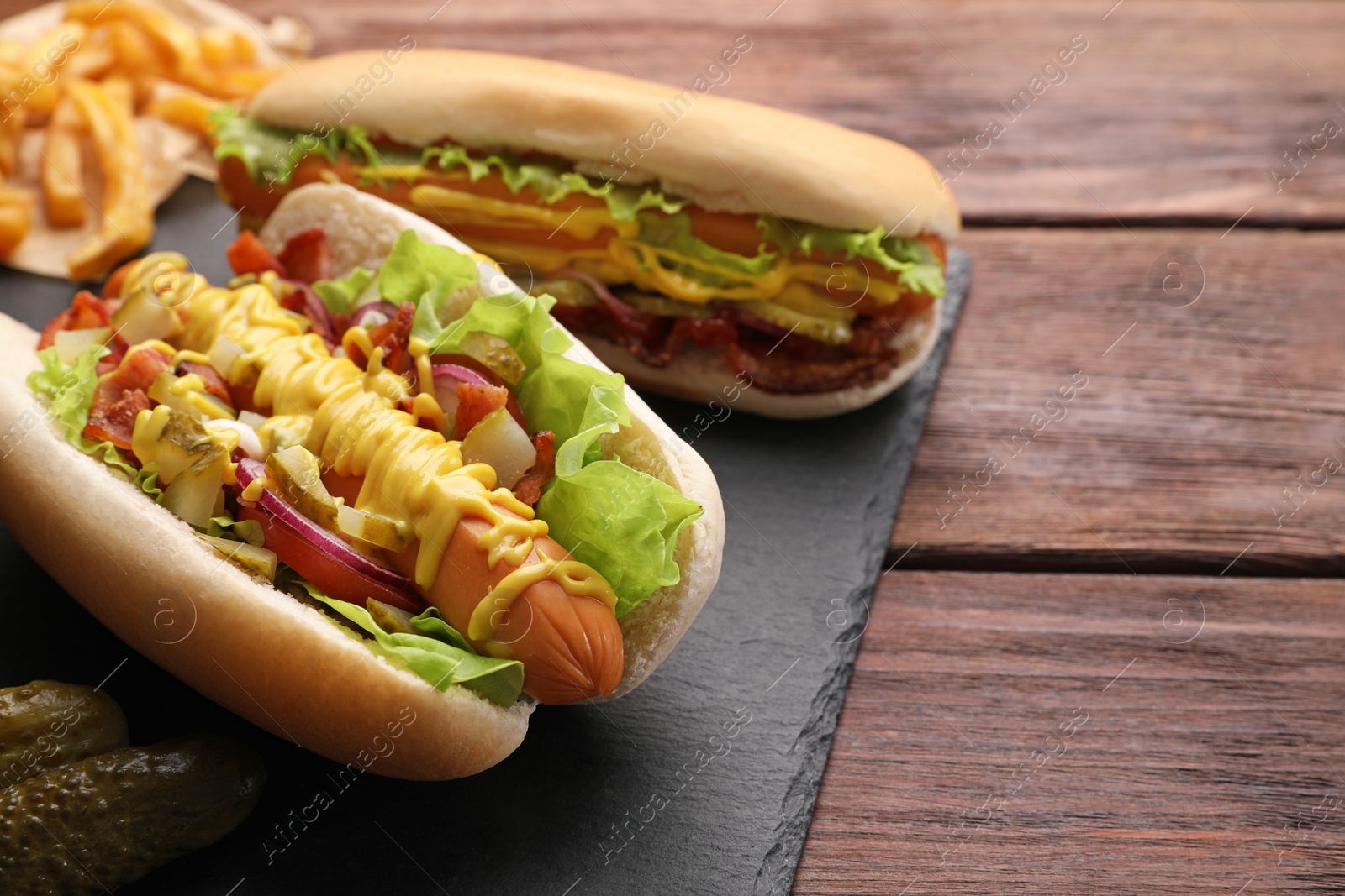 Photo of Delicious hot dogs with lettuce, onion and pickle on wooden table. Space for text