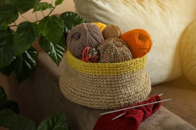 Photo of Soft woolen yarns, knitting and needles on brown sofa indoors