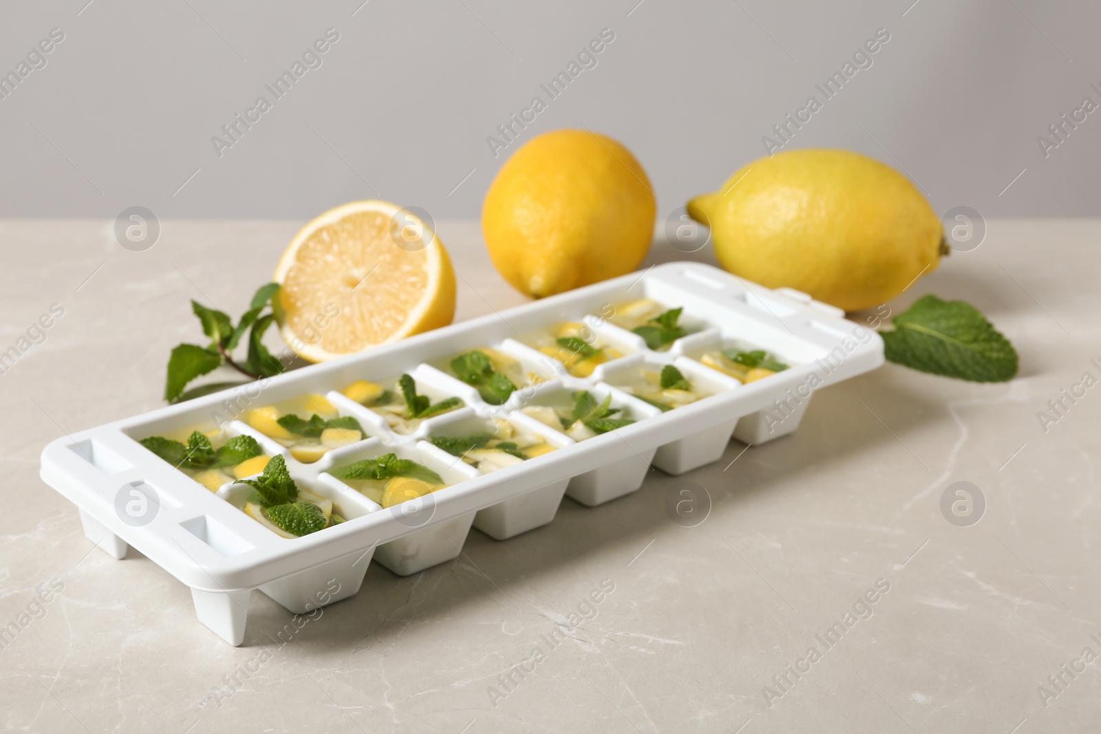 Photo of Ice cube tray with mint, lemon and water on grey table