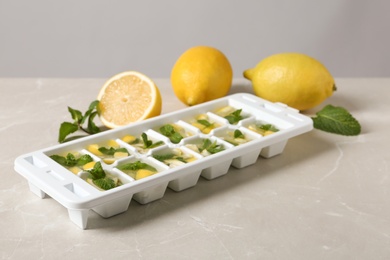 Photo of Ice cube tray with mint, lemon and water on grey table