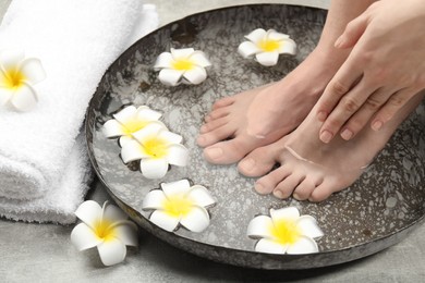 Woman soaking her feet in bowl with water and flowers on light grey floor, closeup. Spa treatment