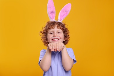 Photo of Portrait of happy boy wearing cute bunny ears headband on orange background. Easter celebration