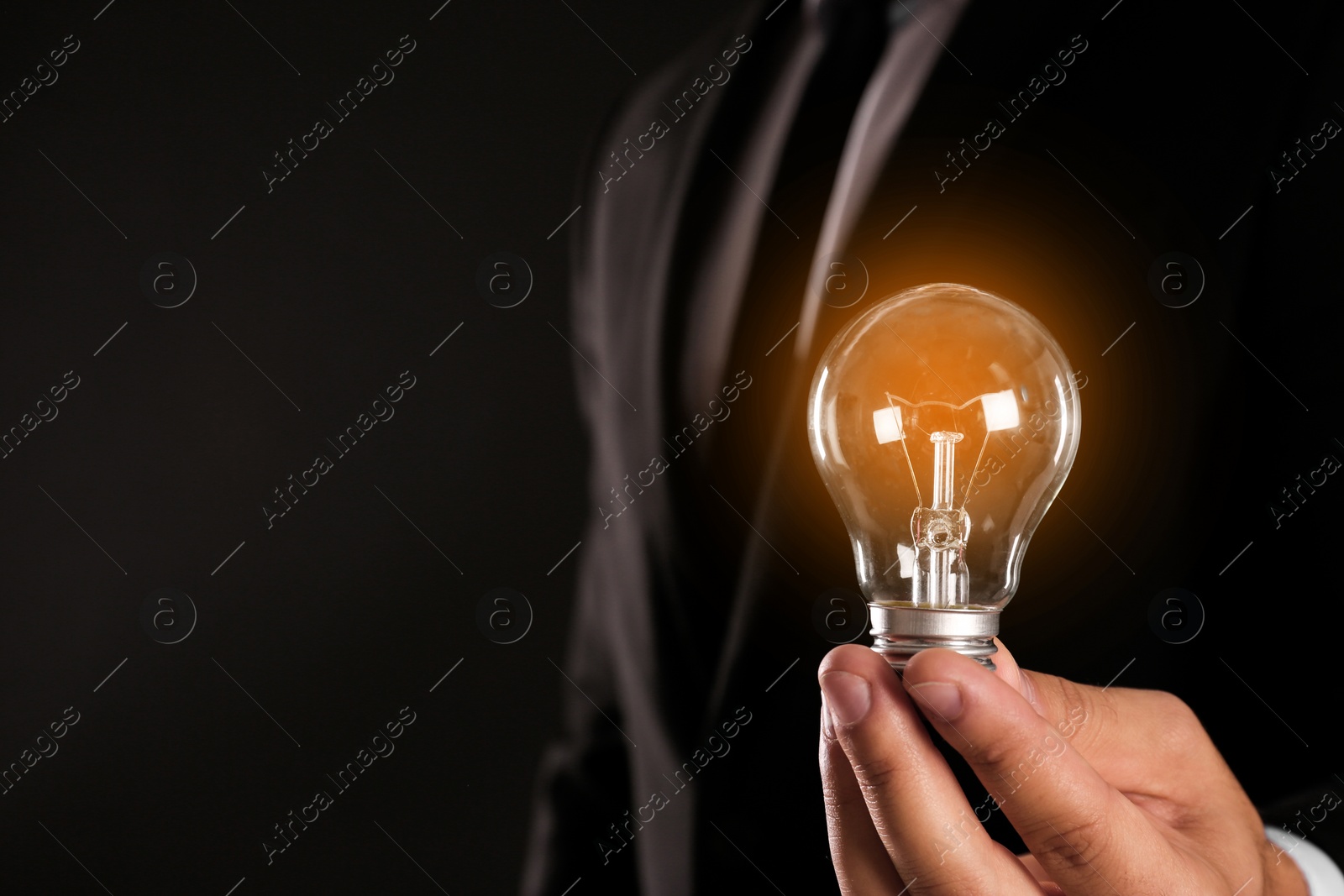 Photo of Businessman holding lamp bulb against dark background, closeup. Space for text