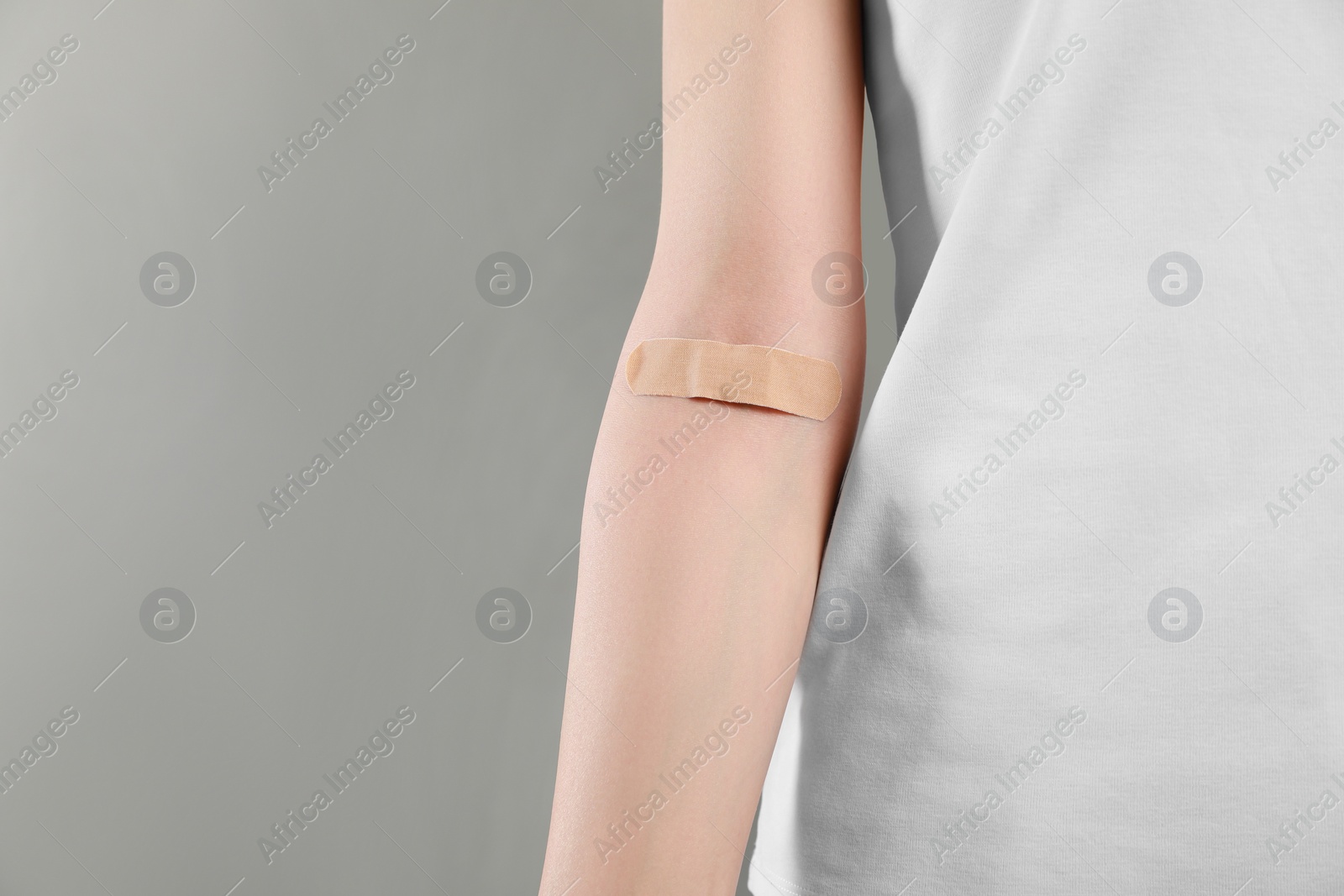 Photo of Blood donation concept. Woman with adhesive plaster on arm against grey background, closeup. Space for text