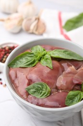 Bowl with raw chicken liver and basil on white textured table, closeup