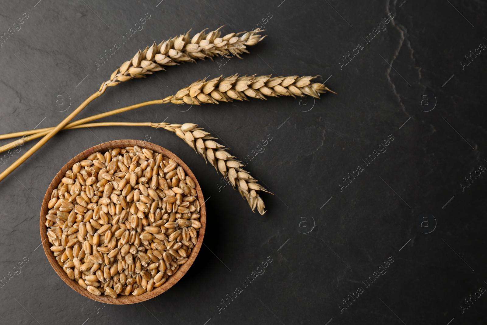 Photo of Dried ears of wheat and grains in bowl on black table. Space for text