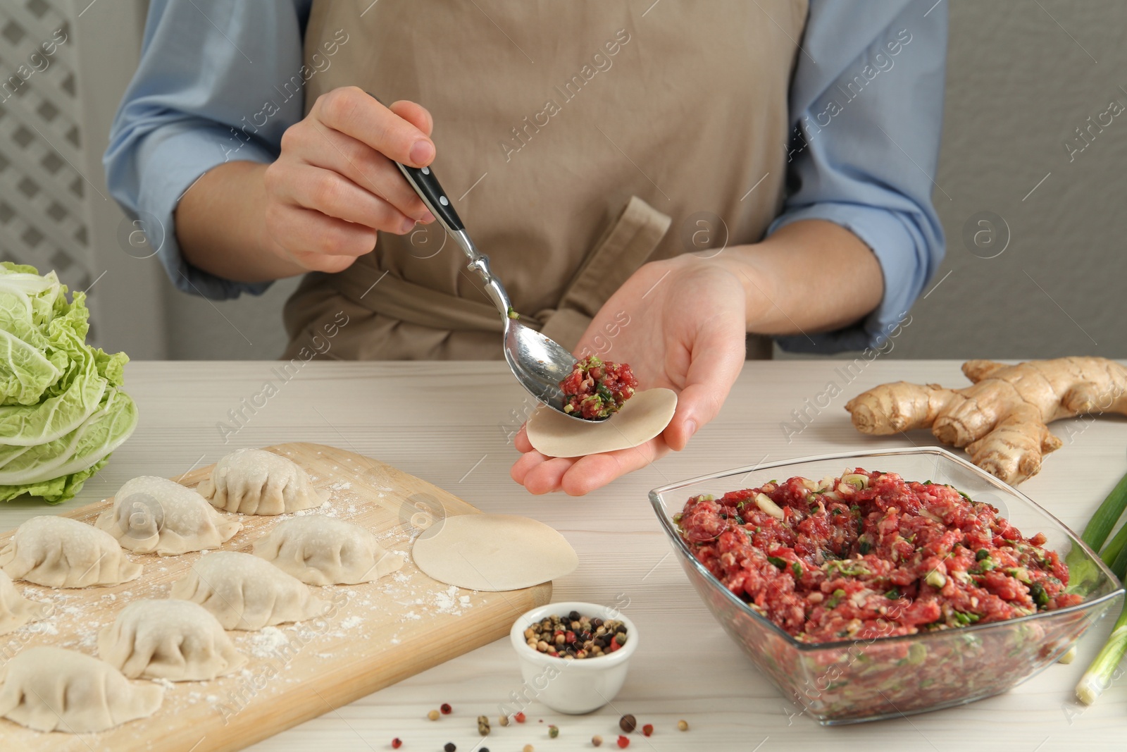 Photo of Woman putting gyoza filling in center of dough wrapper at white wooden table, closeup