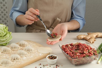 Photo of Woman putting gyoza filling in center of dough wrapper at white wooden table, closeup