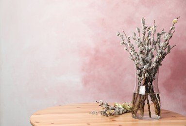 Photo of Beautiful pussy willow branches on wooden table against pink background, space for text