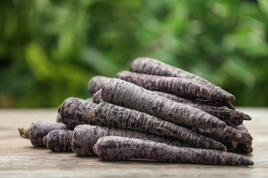 Photo of Raw black carrots on wooden table against blurred background