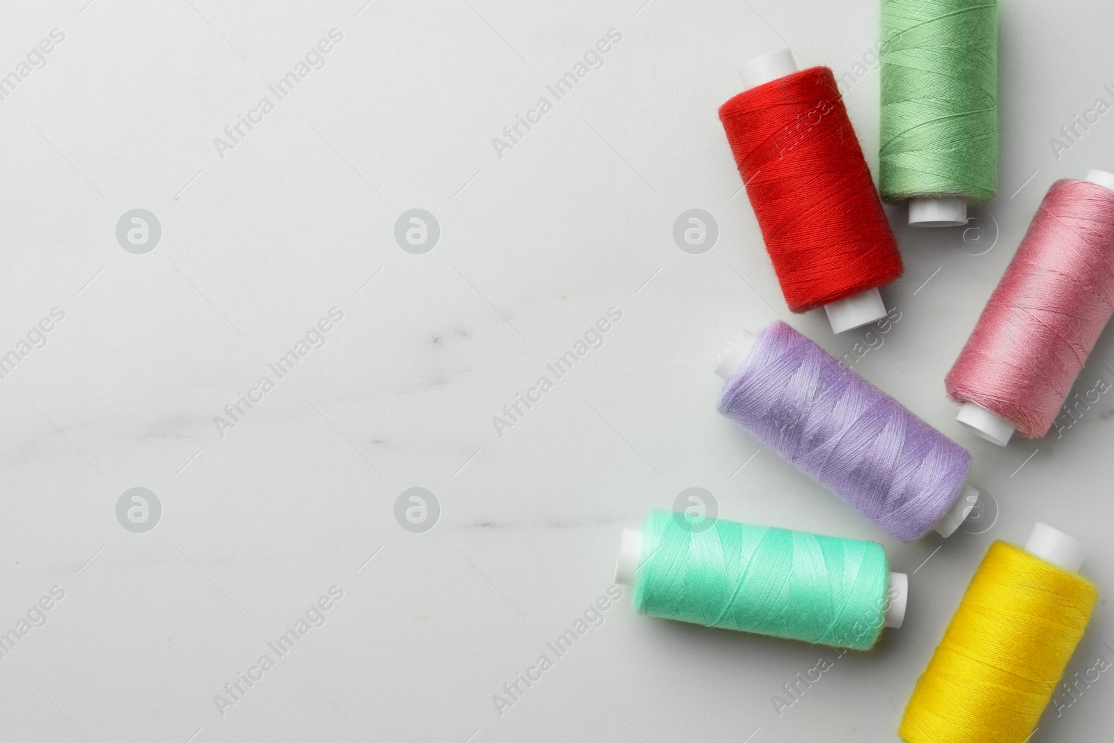 Photo of Colorful sewing threads on white marble table, flat lay. Space for text